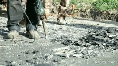 一名建筑工人用手提钻在路上打散沥青